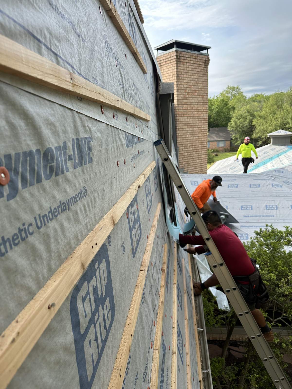Synthetic underlayment rolled across the roof, crew on ladders