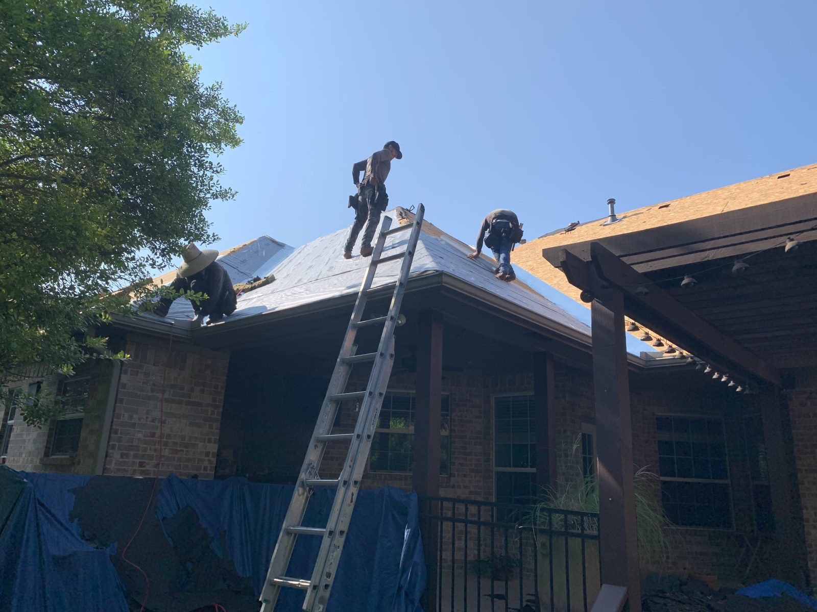 A Big Bob’s Roof Pros crew laying underlayment on a brick home under a clear Texas sky